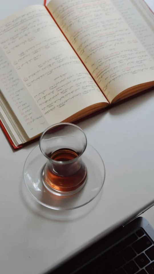 An open notebook beside a glass of tea on a desk